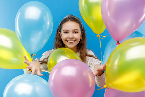 Cute little emotional girl in white clothing with colored ballons on blue background. - Fotó, kép