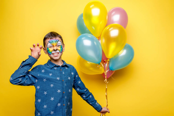 Happy boy with aquagrim on birthday party, colorful tiger holding colorful balloons isolated on yellow background. - Φωτογραφία, εικόνα