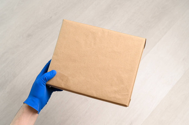 couriers hand in rubber glove holds cardboard parcel box - Photo, Image