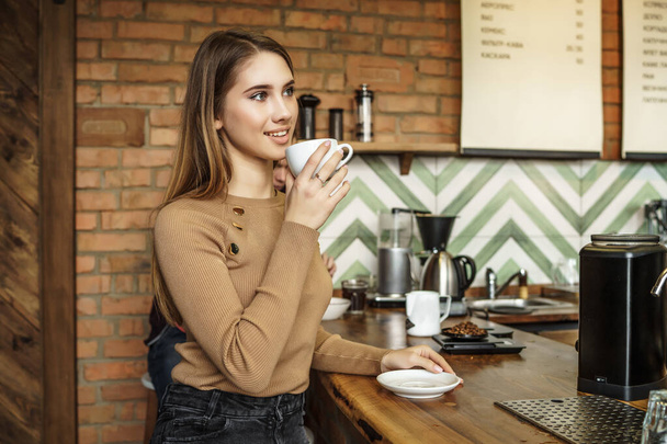 Portrait of young woman, customer and lady, sitting ner bar counted and drinking coffee. - Photo, Image