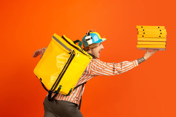 Contacless delivery service during quarantine. Man delivers food and shopping bags during insulation. Emotions of deliveryman isolated on orange background. - Fotoğraf, Görsel