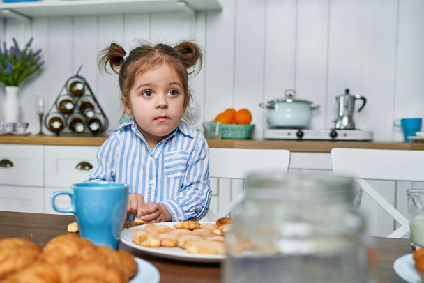 The kid in the kitchen wants to eat cookies with tea at home - Fotoğraf, Görsel