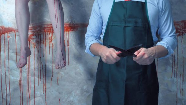 man with a knife on the background of the bloody walls and the hanging legs - Foto, afbeelding