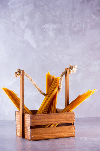 Pasta in a wooden box. Donation wooden box with raw spaghetti on a gray background. Social assistance with food. Safe food delivery. Food donation concept. Copy space - Φωτογραφία, εικόνα