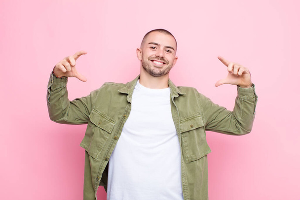 young handsome man framing or outlining own smile with both hands, looking positive and happy, wellness concept against flat wall - Фото, зображення