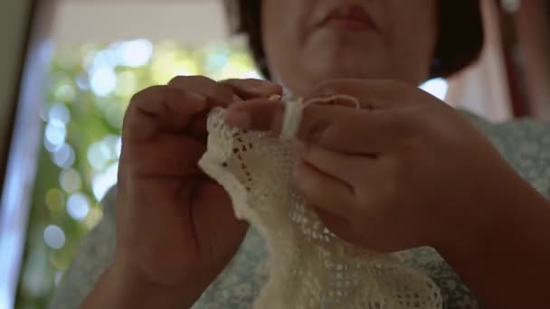 Eine ältere Frau in asiatischen Frauenkleidern sitzt strickt und häkelt im Haus, ein Hobby, das zarte Handwerkskunst ist.. - Filmmaterial, Video