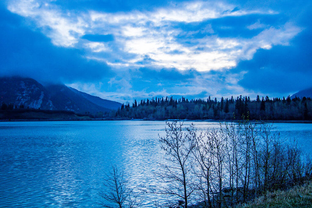 Ο ήλιος ανατέλλει και τα χαμηλά σύννεφα αιωρούνται πάνω από τη λίμνη. Lac de Arc, Αλμπέρτα, Καναδάς - Φωτογραφία, εικόνα