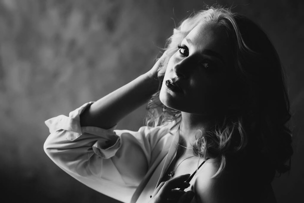 Portrait of a beautiful young blonde girl in low key. Black and white art photo. Soft selective focus. - 写真・画像