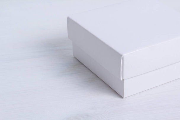 Closed white gift box with a lid on isolated wooden background. Crop image, side view, square box. Elegant eco-friendly mockup. Isolated box with cover on white wooden table. Empty space on the left. - Foto, imagen