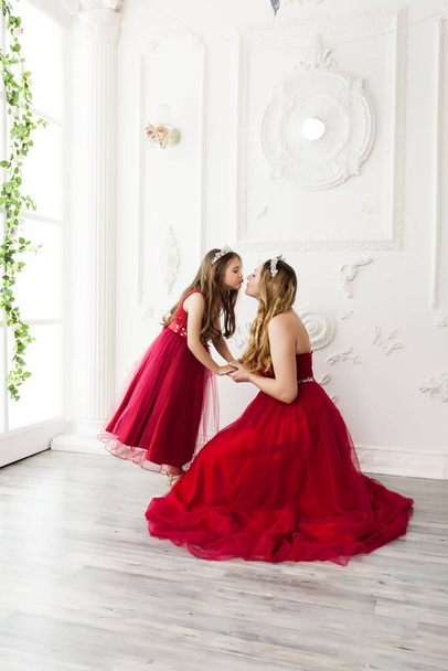 Mother and daughter in same outfits posing in the interior of the photo studio weared Red Dresses. Family look - Photo, image
