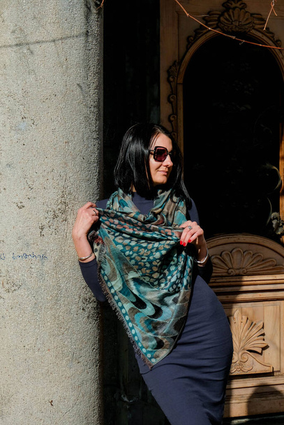 Moda, mujer morena en vestido y bufanda en la calle. Disfruta de un soleado día de primavera. Modelo chica posando en Batumi, Georgia. Ciudad vieja en el fondo. - Foto, imagen