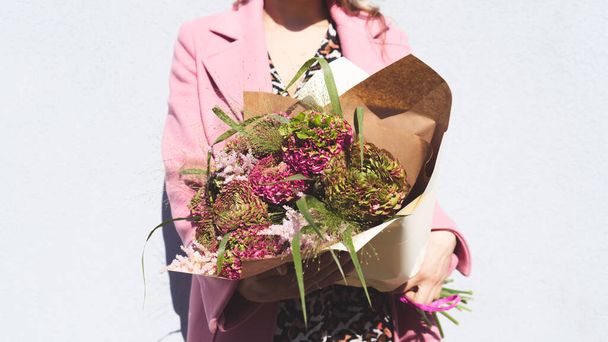 Muotokuva kaunis nuori nainen malli tilalla eksoottisia kukka kukkakimppu. Houkutteleva sekarotuinen nainen poseeraa kukkien kanssa aurinkoisena päivänä
. - Valokuva, kuva