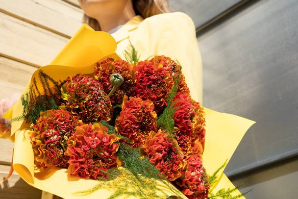 Elegáns nő kezében gyönyörű és egzotikus virág buquet a kezében. Sárga, piros és narancssárga ranunculus csokor közelről. Virágos téma. - Fotó, kép