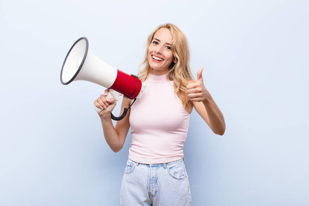 young blonde woman feeling proud, carefree, confident and happy, smiling positively with thumbs up with a megaphone - Foto, Imagem