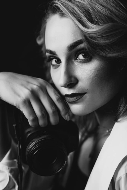 Portrait d'une belle femme photographe avec un appareil photo dans les mains en mode discret. Photo d'art en noir et blanc. Concentration sélective douce
. - Photo, image