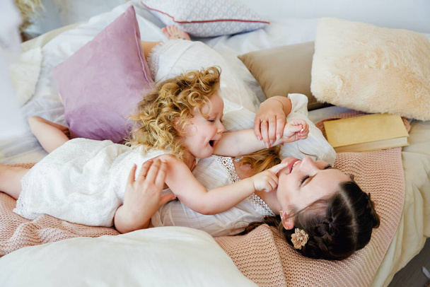 Happy loving family. Mother and daughter play and hug. The morning together. Happy games in the bedroom. - Фото, зображення