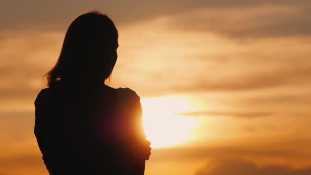 Silhouet van een jonge pensieve vrouw bij zonsondergang kijkend in de verte - Video