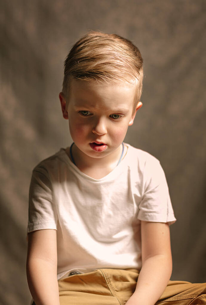 sad boy in a white t-shirt is sitting on a chair. Retro style photo - Foto, Imagem