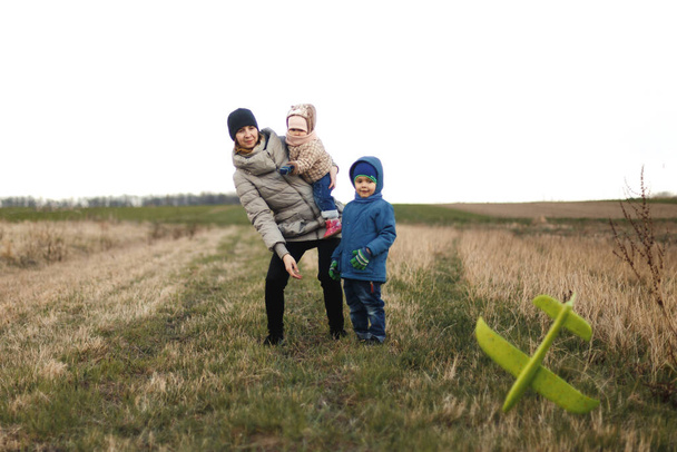 Jovem mãe com dois filhos, uma menina e um menino brincando no campo de outono. Família de outono no parque brincando com avião de brinquedo
. - Foto, Imagem