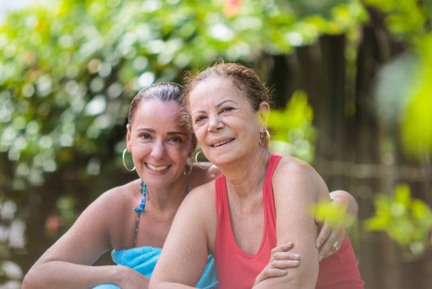 mother and daughter holding each other and smiling, narrow focus, blurred garden background, - Photo, Image
