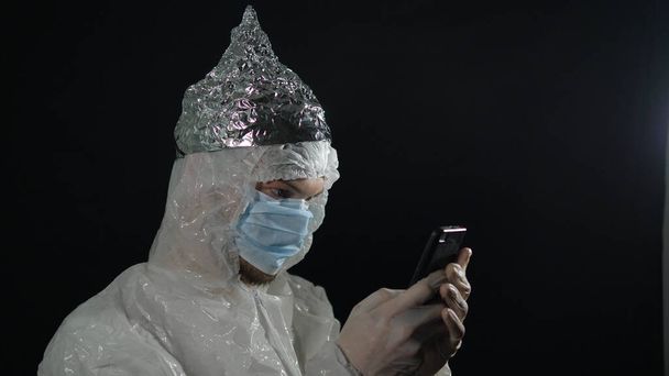 5G kule radyasyon koruması, folyo kapaklı genç bir adam akıllı telefona yakından bakıyor. - Fotoğraf, Görsel