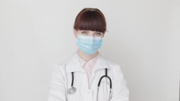Happy smiling female doctor, scientist wearing white coat, stethoscope and medical face mask looking at camera on white background, winking and showing thumb up gesture. Stop covid-19 pandemic - Materiał filmowy, wideo