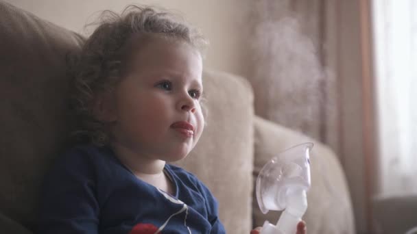 Onnellinen hauska lapsi kohtelee flunssaa hengittämällä hengitysteitse höyryä. Pikkutyttö, jota on hoidettu naamarilla.
. - Materiaali, video
