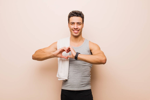 young arabian man smiling and feeling happy, cute, romantic and in love, making heart shape with both hands. sport concept - Фото, зображення