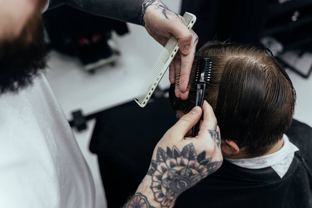 Ammattimainen tatuoitu parturi leikkaamalla hiuksia. Houkutteleva mies käy parturissa parturissa. Sulje se.
. - Valokuva, kuva