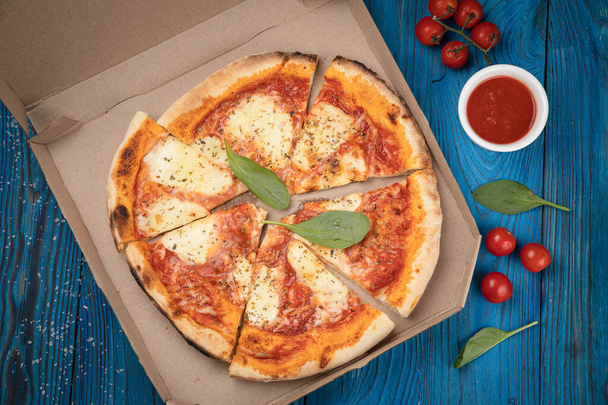 Pizza in a cardboard box on a wooden board. Pizza delivery - Foto, afbeelding
