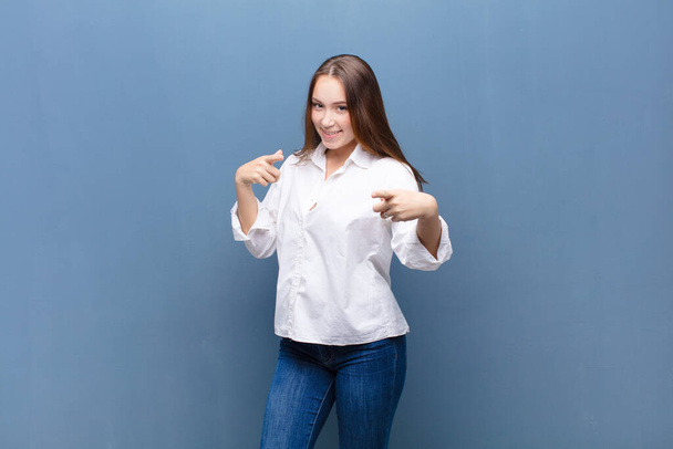 young blonde pretty girl smiling with a positive, successful, happy attitude pointing to the camera, making gun sign with hands against concrete wall - Fotoğraf, Görsel