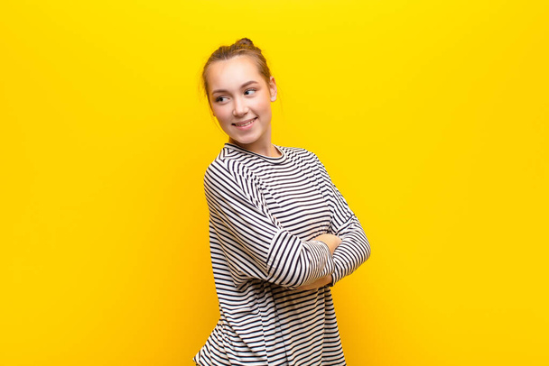 young blonde pretty girl thinking or doubting, scratching head, feeling puzzled and confused, back or rear view against yellow wall - Fotoğraf, Görsel