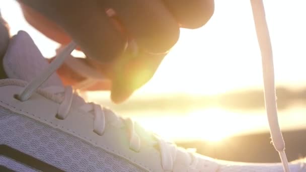 A kezek cipőfűzőt kötnek a futócipőre, mielőtt kocognának a naplemente hátterében. Közelíts a futócipőkre. Lassú mozgás.. - Felvétel, videó
