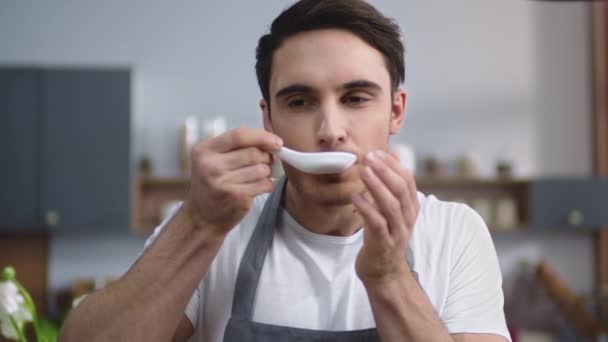Portrait of man cook tasting fresh soup at home kitchen. Male chef cooking meal - Felvétel, videó