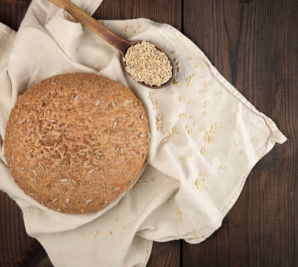 baked round rye bread with sunflower seeds on a beige textile napkin, wooden background, top view - Foto, afbeelding