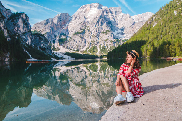 žena v červených kostkovaných šatech se slamákem při pohledu na horské jezero. letní prázdniny. cestovní koncept - Fotografie, Obrázek