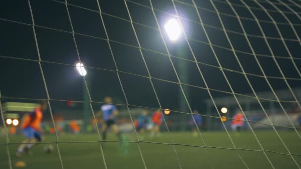 Partita di football serale. Giocatori di calcio giocano sul campo di allenamento, illuminato da luci dello stadio. Vista attraverso la rete degli obiettivi
. - Filmati, video