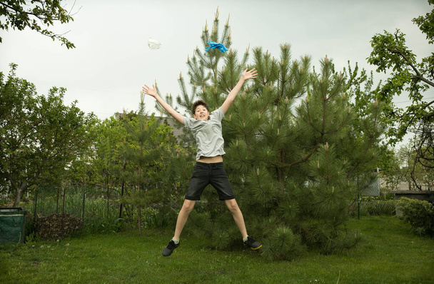 La alegría de un joven en la naturaleza después de la cuarentena. El niño salta de alegría y tira máscaras y guantes médicos innecesarios
. - Foto, imagen