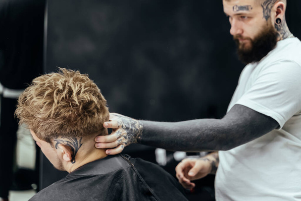 Barber makes hair styling with hair gel and comb after haircut at the barber shop. Young handsome Caucasian man getting a haircut in a modern hairsalon - Photo, Image