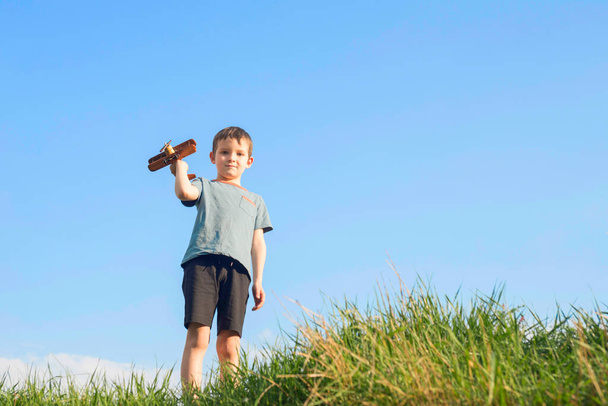 Mały chłopiec bawi się drewnianym samolotem. Dziecko trzyma zabawkę drewniany samolot. - Zdjęcie, obraz