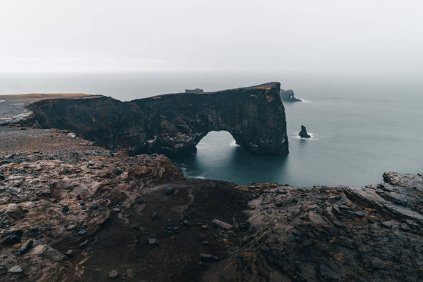Słynna skała o nazwie Dyrholaey znajduje się w Islandii w pobliżu miasta Vik. Ta skała jest bardzo popularnym celem dla fotografów w każdych warunkach pogodowych - Zdjęcie, obraz