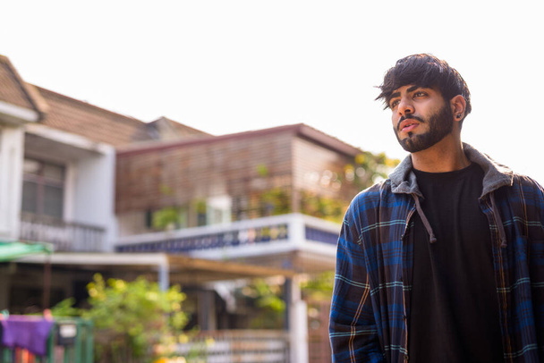Portrait of young handsome bearded Indian hipster man in the streets outdoors - Photo, Image
