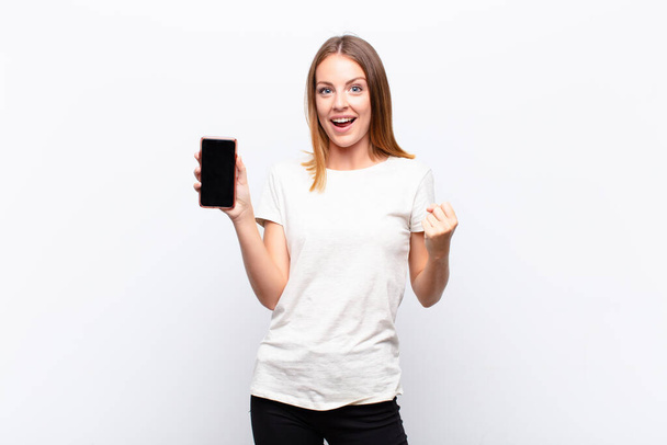 red head pretty woman feeling shocked, excited and happy, laughing and celebrating success, saying wow! holding a smartphone - Foto, Bild