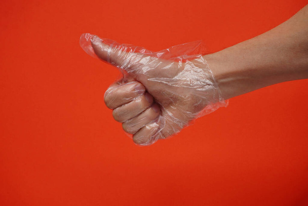 Bir el plastik ya da plastik kaplı tek kullanımlık eldivenler kırmızı arka planda. Koronavirüs pandemiği sırasında virüslere ve bakterilere karşı korunma. İşareti, kopyalama alanını, tamam veya işaret kavramını parmakla. - Fotoğraf, Görsel