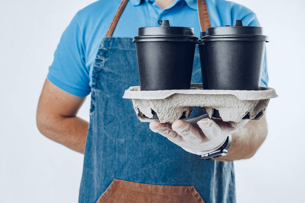 Man coffee shop worker giving takeaway cups of coffee on grey background - Photo, image