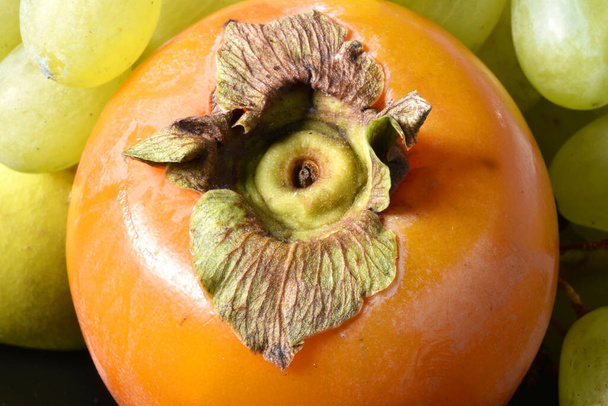 An orange persimmon with some white grapes: typical Italian autumn fruits. - Photo, Image