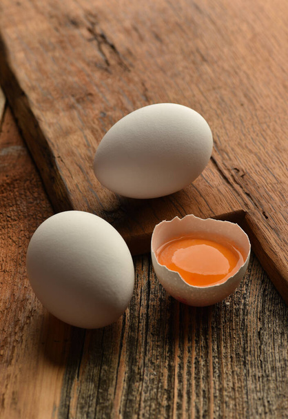 Chicken eggs and half broken egg with yolk on wooden background - Zdjęcie, obraz
