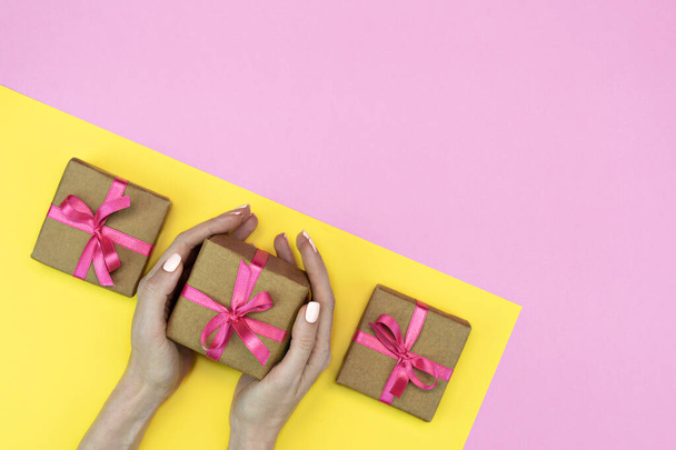 flatlay de caixas de presente de presente com fita rosa, flores de orquídea em fundo amarelo rosa com as mãos femininas. lidar com o espaço
 - Foto, Imagem