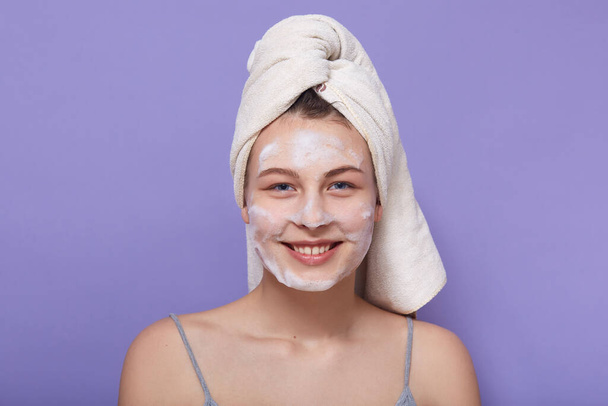 Closeup portrait of smiling happy female posing wrapped in white towel, looking directly at camera, posing isolated over lilac background. Skincare, cosmetology, morning procedures, spa concept. - 写真・画像
