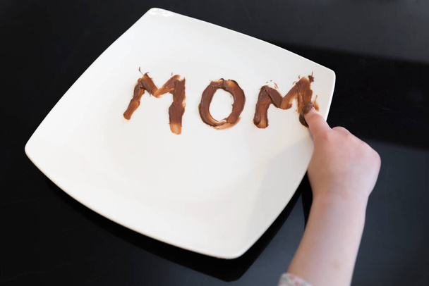 The word mom written on a plate with chocolate spread by her young daughter - Fotoğraf, Görsel